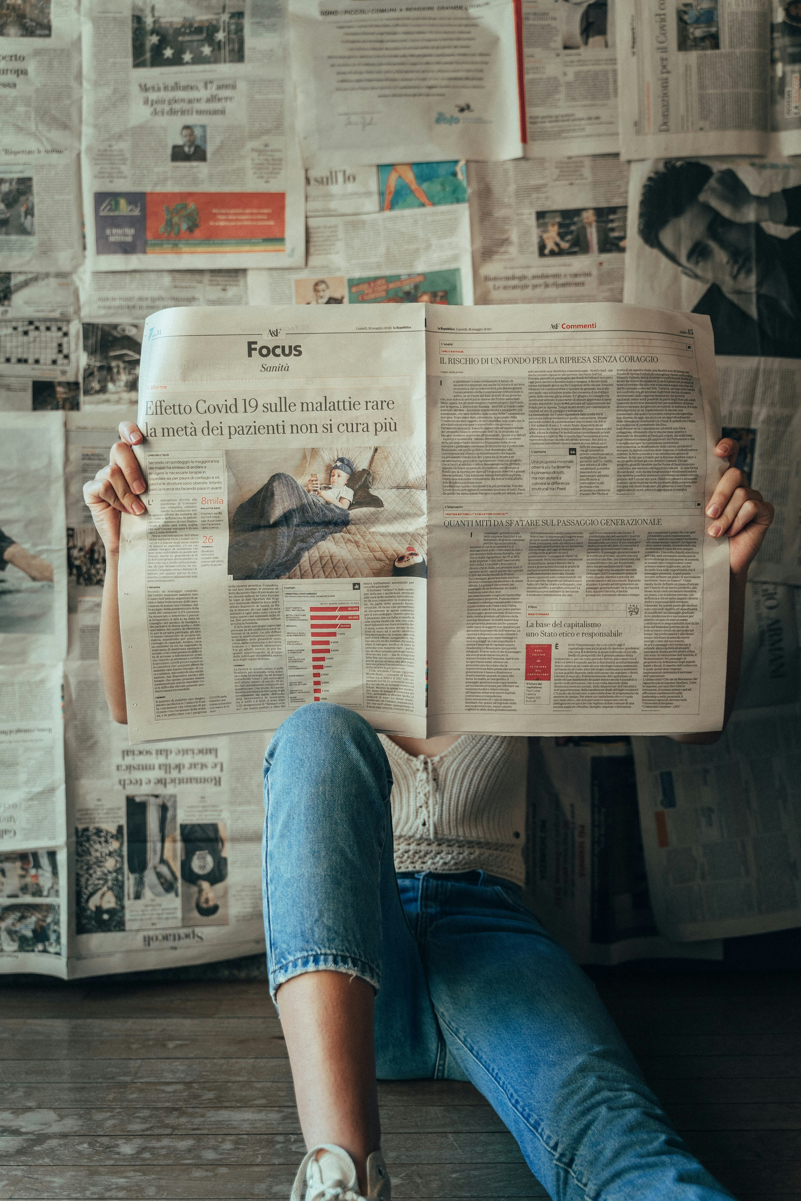 Someone reads a newpaper, with the wall behind them covered in newspapers.